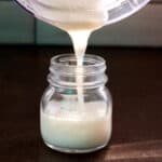Pouring coconut butter into a small glass jar from a food processor container