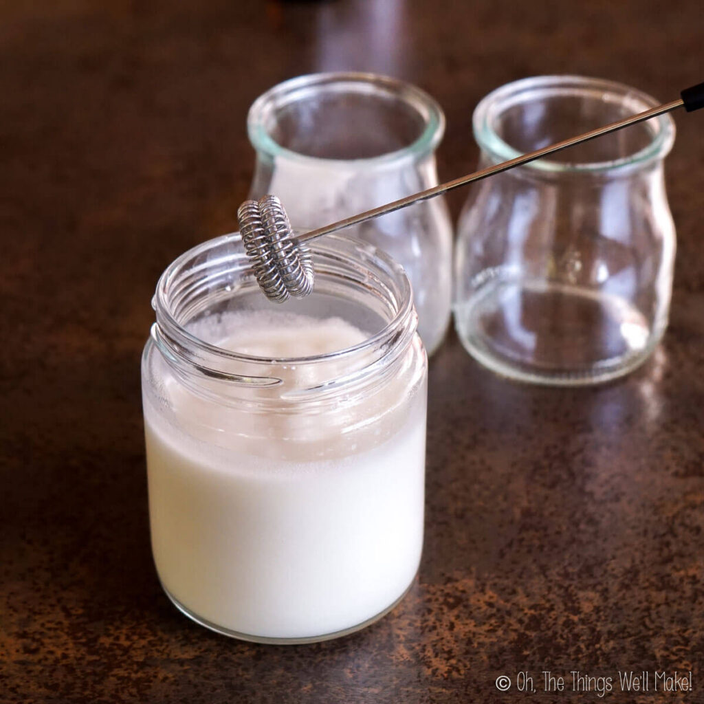 A white lotion in a jar with a milk frother over it.