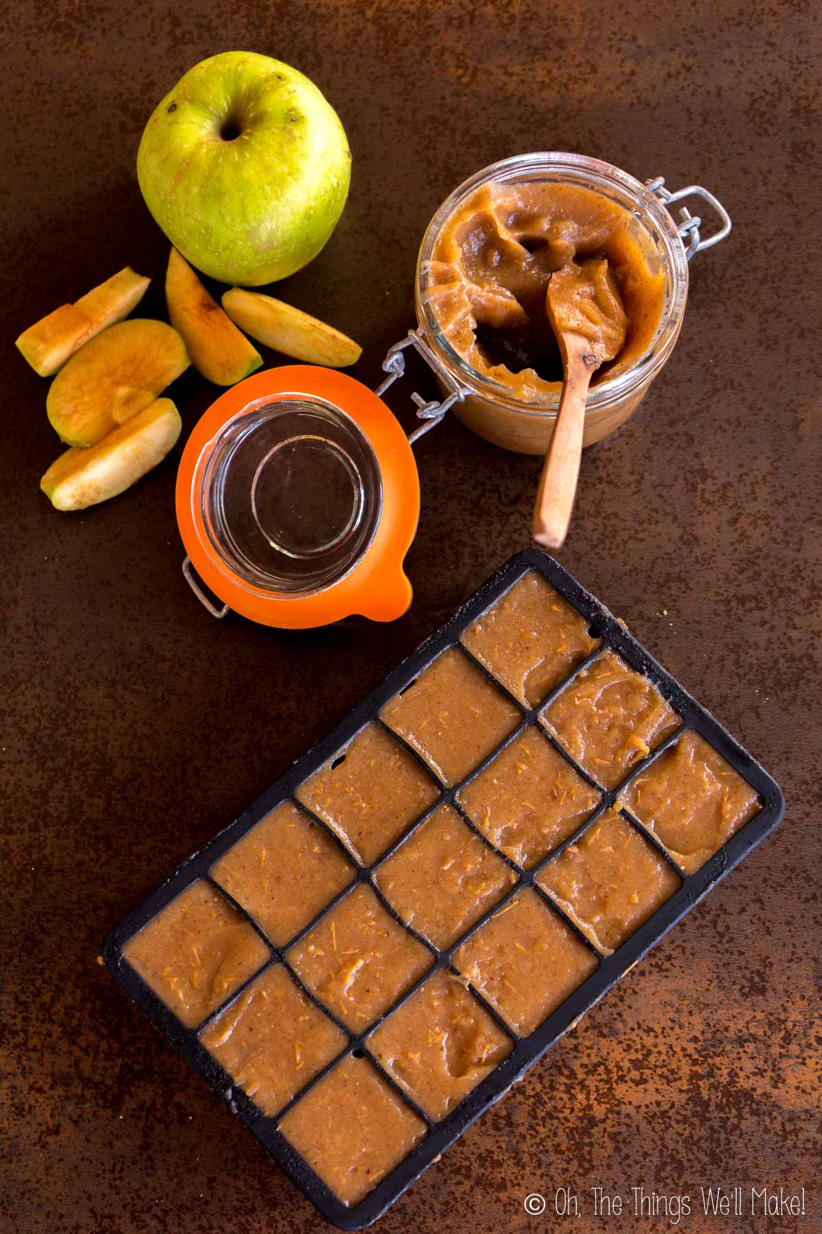 Homemade apple butter in an ice cube tray for freezing individual portions, alongside a jar of apple butter and a green apple.