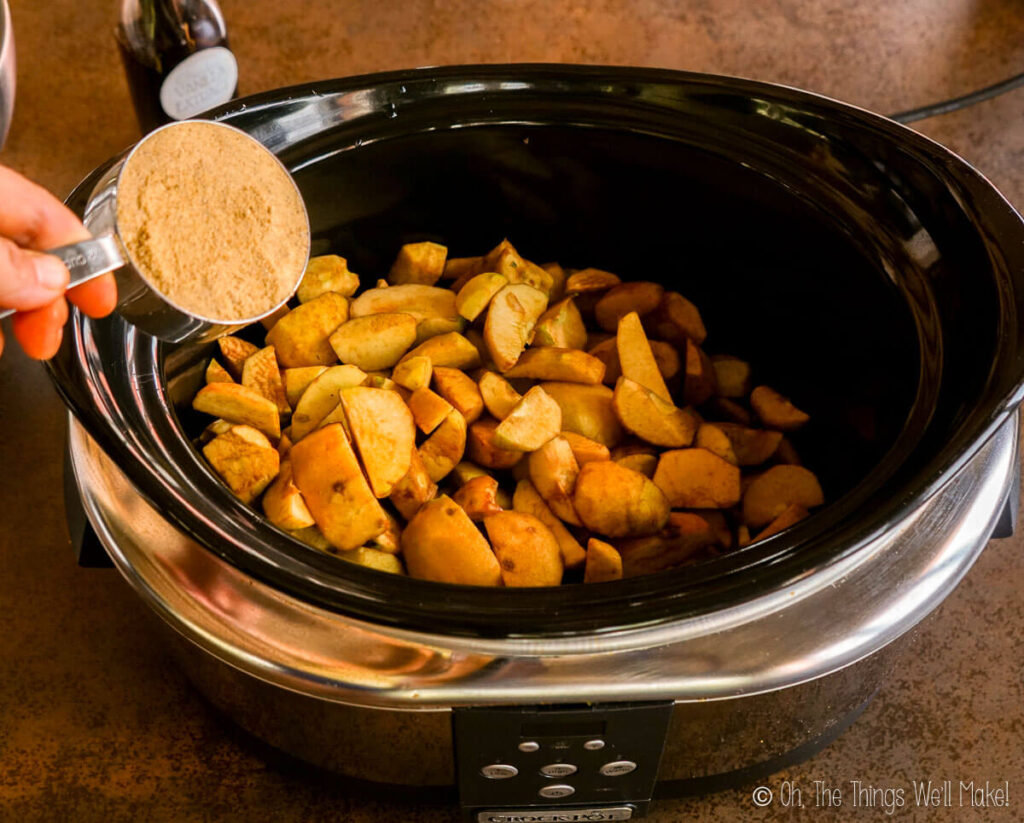 Adding brown sugar to a slow cooker filled with apple pieces