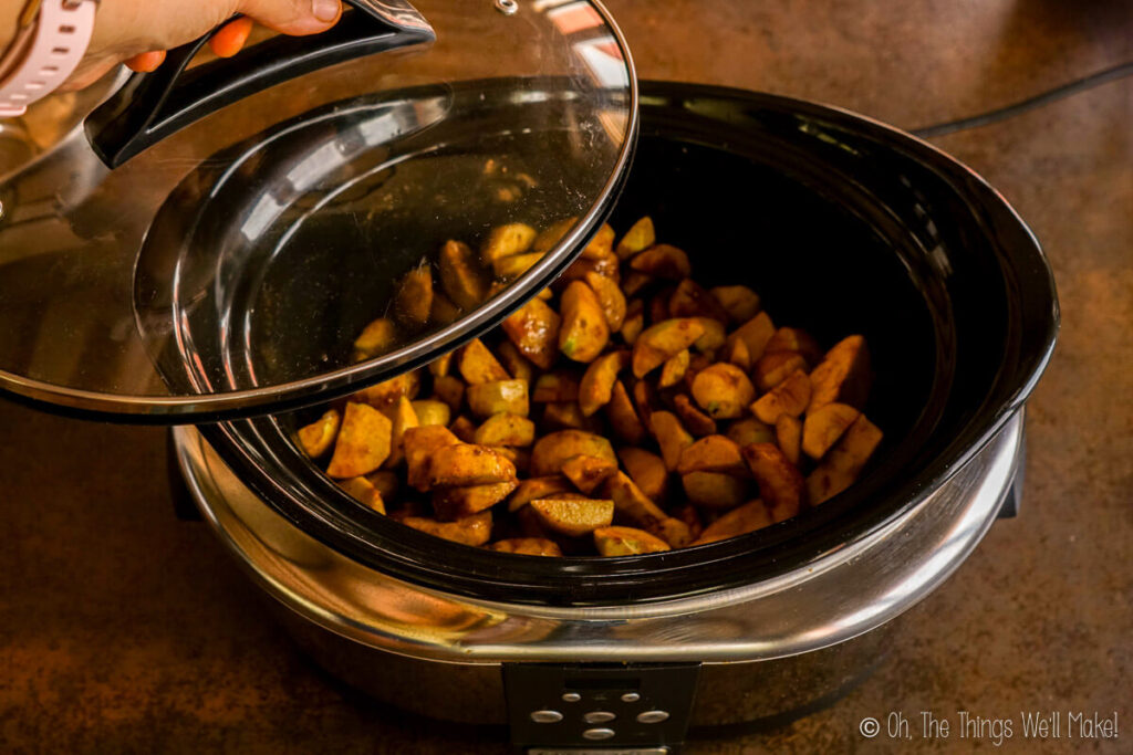 Placing a lid on a slow cooker filled with apple pieces