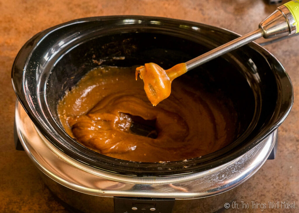 An immersion blender over apple butter in a slow cooker