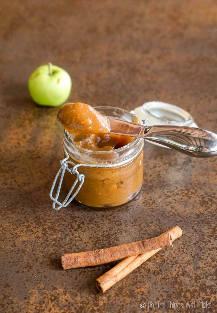 Closeup of homemade apple butter on a cheese spreader over a jar of apple butter.