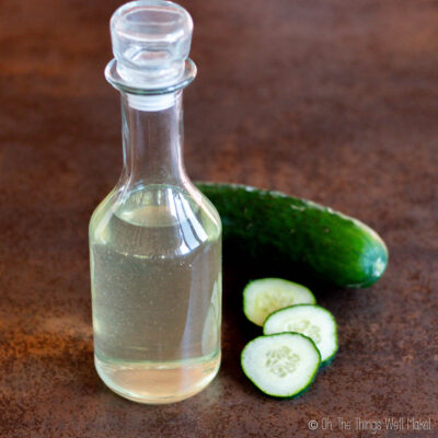 homemade cucumber extract in a bottle near a cucumber and some cucumber slices.
