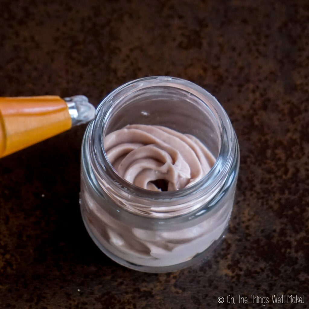 piping a purple body butter into a jar