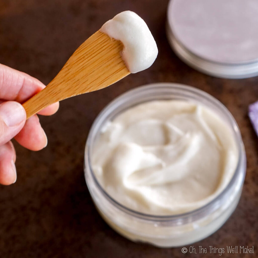 holding some body butter on a spatula over a jar of body butter