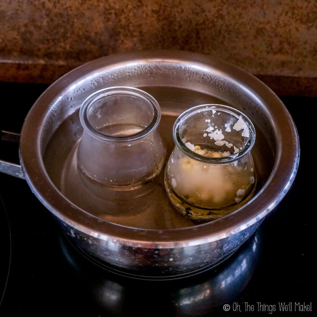 Two glass jars filled with water and oil phase ingredients in a saucepan filled with water