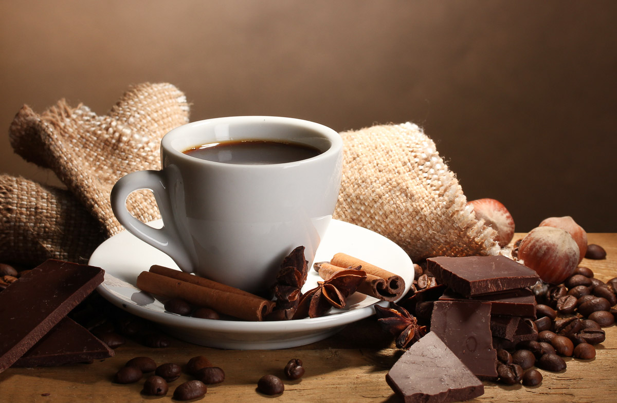 coffee surrounded by cinnamon sticks, star anise, chocolate pieces, and coffee beans.