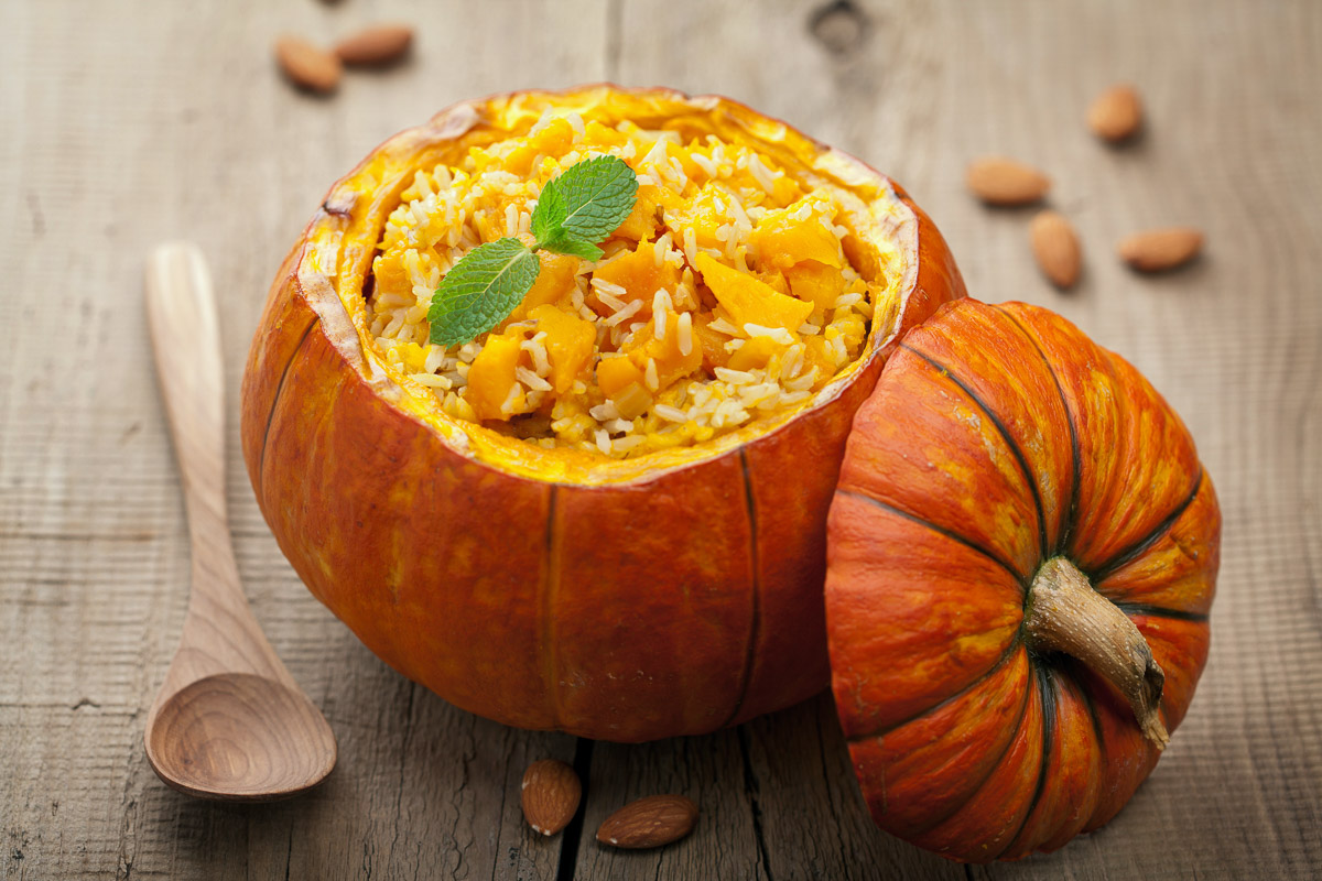 A hallowed out pumpkin being used as a bowl for a vegetable rice dish.