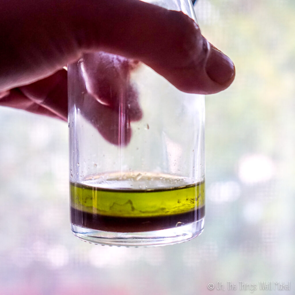 holding up a glass with olive oil to the light, showing a small amount of dark liquid below