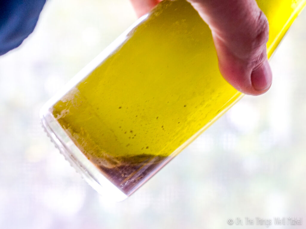 holding a bottle of olive oil on an angle with a dark olive juice in the bottom part. 