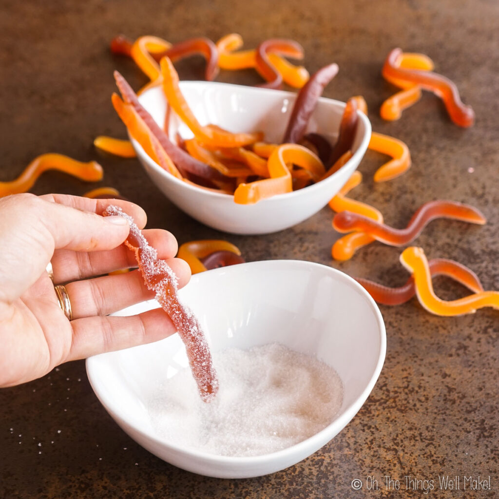 dipping a homemade gummy worm into a bowl of citric acid and sugar mixture