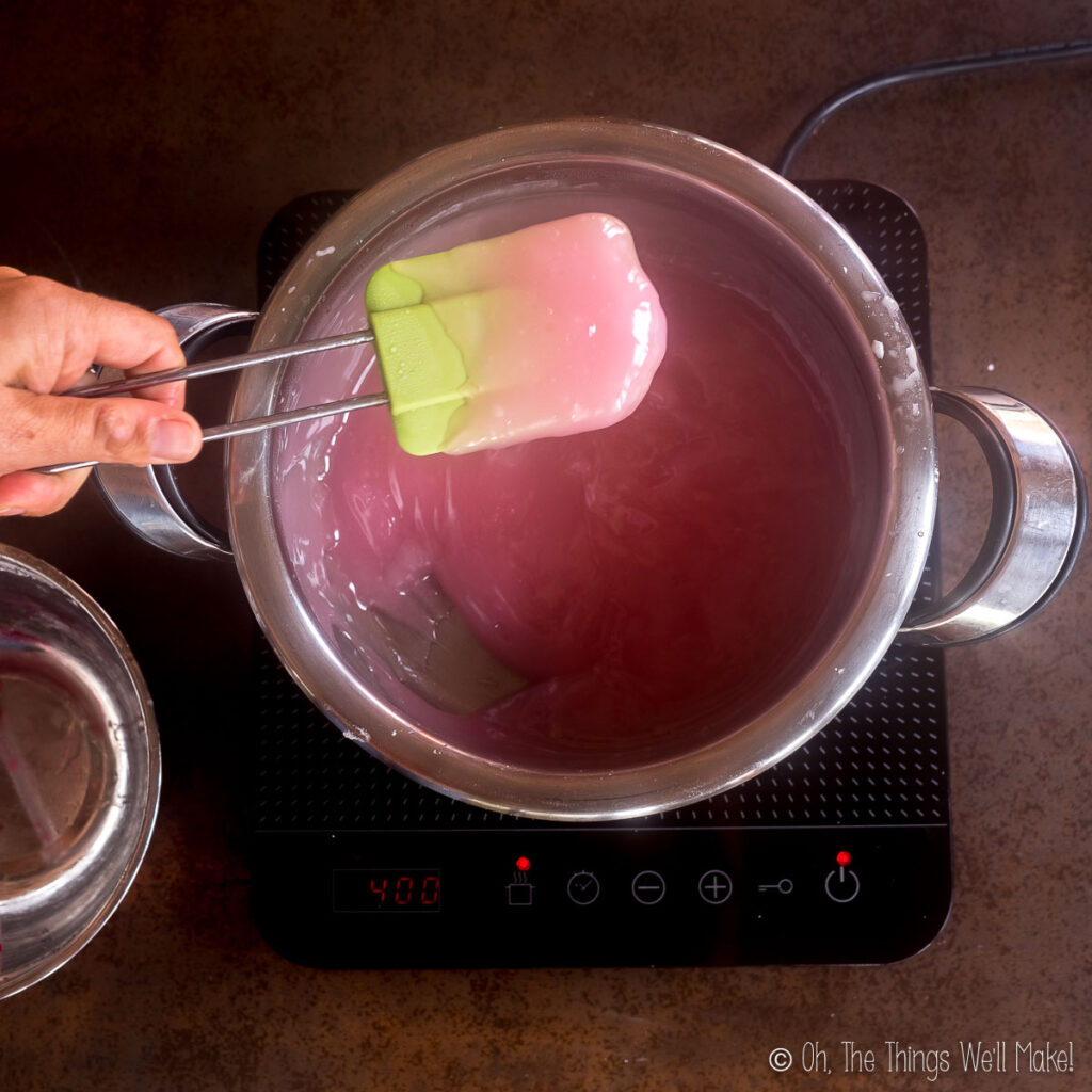 holding up a slightly thickened pink mixture on a spatula