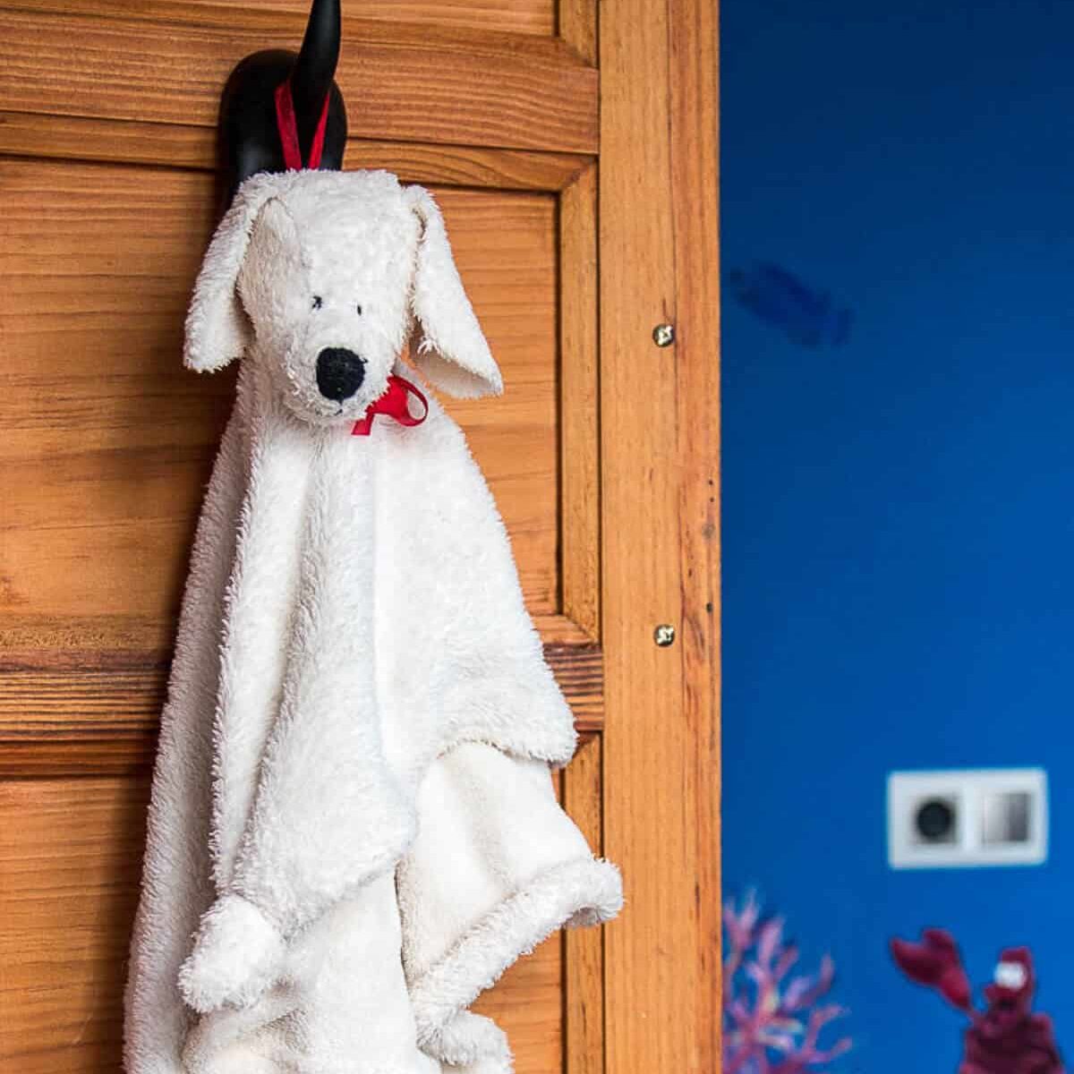 A white fluffy puppy blanket with a stuffed puppy head hanging from the hook on a wood closet door.