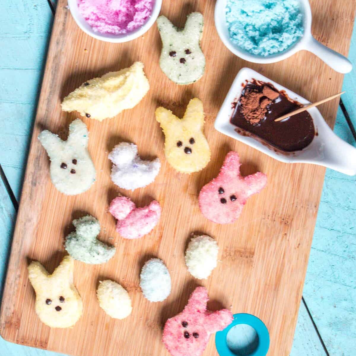 Overhead view of homemade marshmallow peeps covered with naturally colored sugar crystals on a bamboo cutting board.