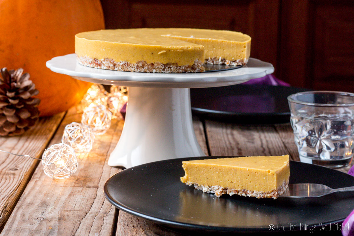 A slice of pumpkin pie on a plate in front of the rest of the pie