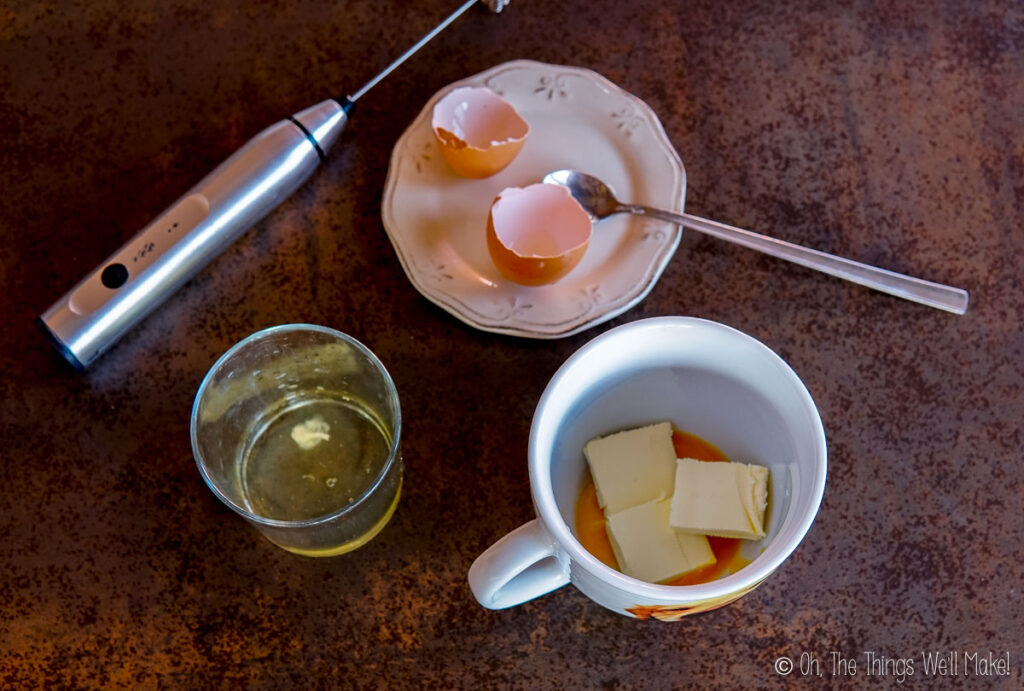 A glass with an egg white next to a mug with butter and an egg yolk.