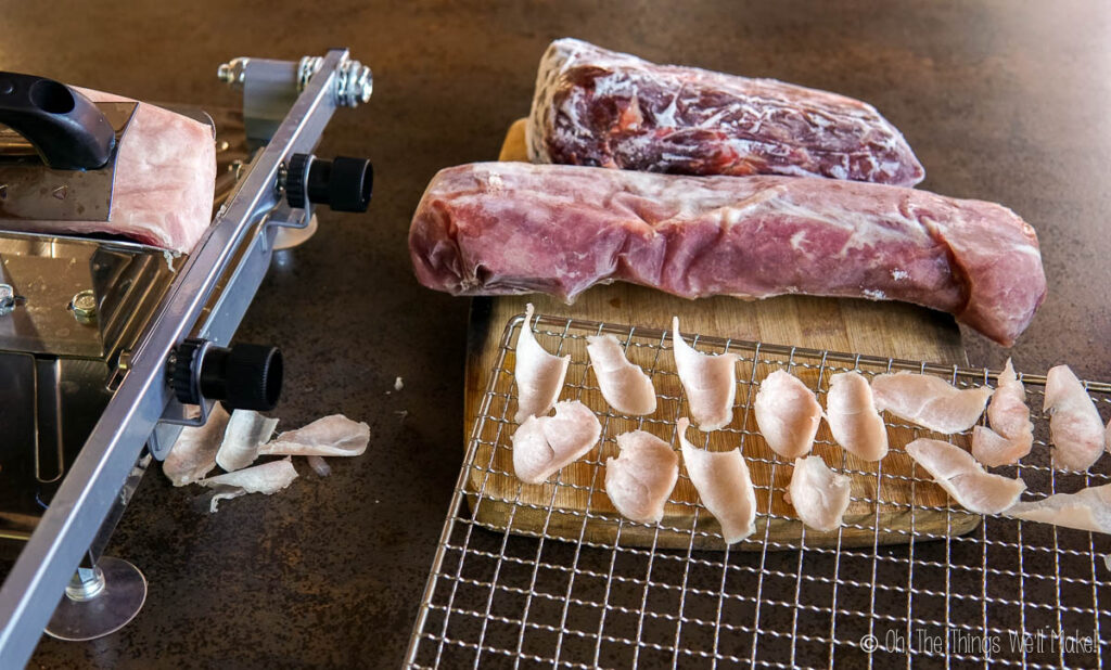 Slicing turkey with a frozen meat slicer with slices of turkey on a dehydrator tray.