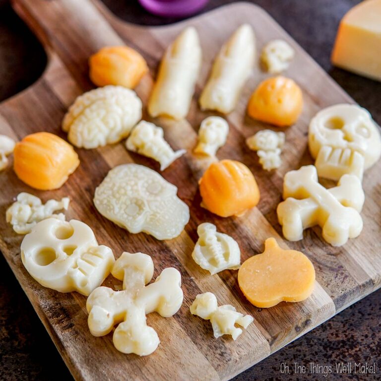 Assorted Halloween-themed cheese shapes, including skulls, pumpkins, and bones, arranged on a wooden board.