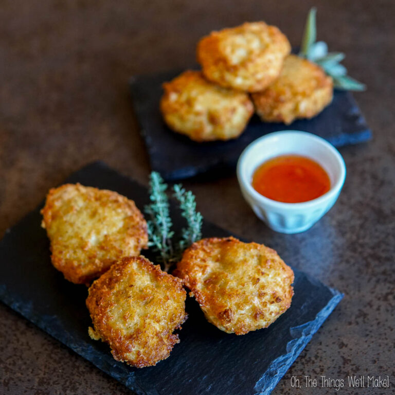 Three keto chicken nuggets rest on a slate with herbs, accompanied by a small bowl of orange sauce. In the background, four more keto chicken nuggets .