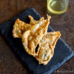 Three crispy chicken skins on a dark slate, accompanied by a chicken schmaltz.