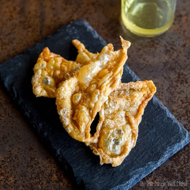 Three crispy chicken skins on a dark slate, accompanied by a chicken schmaltz.