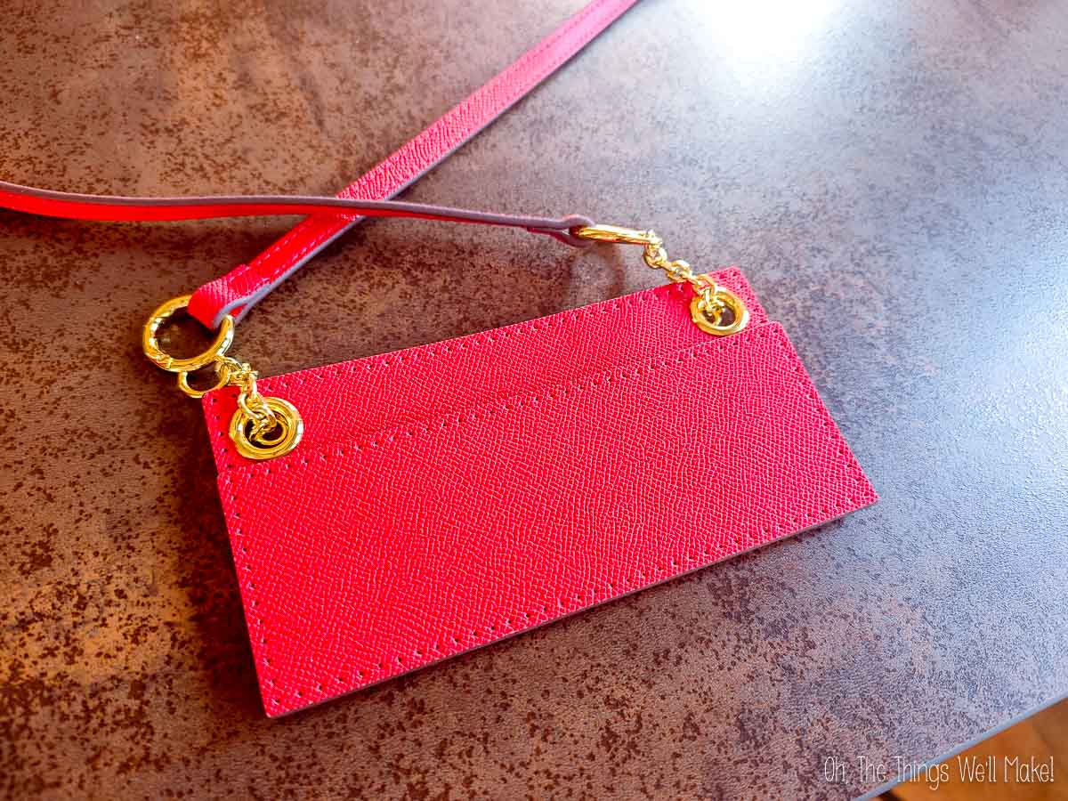 Red envelope-style cardholder with a gold chain, resting on a brown surface.