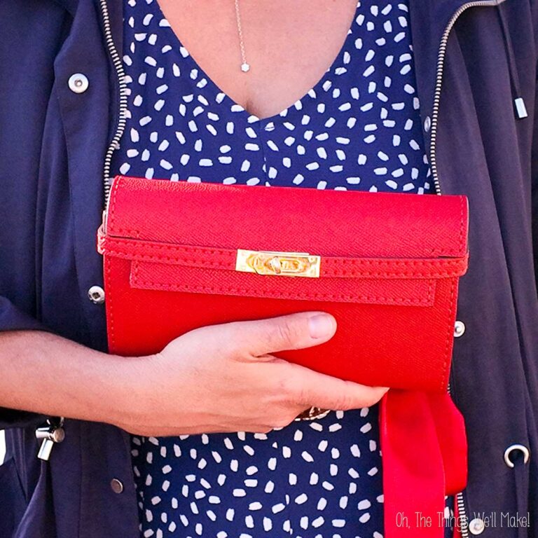 Person holding a red clutch purse in front of a blue and white patterned dress.