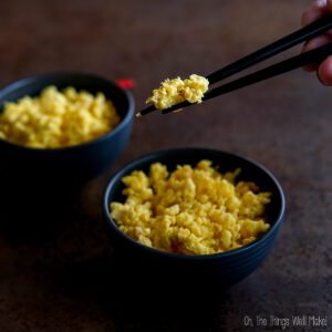 Two black bowls filled with carnivore rice, with a hand using chopsticks to pick up some from one bowl.