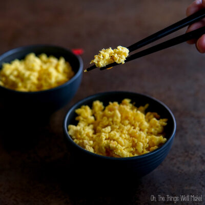 Two black bowls filled with carnivore rice, with a hand using chopsticks to pick up some from one bowl.