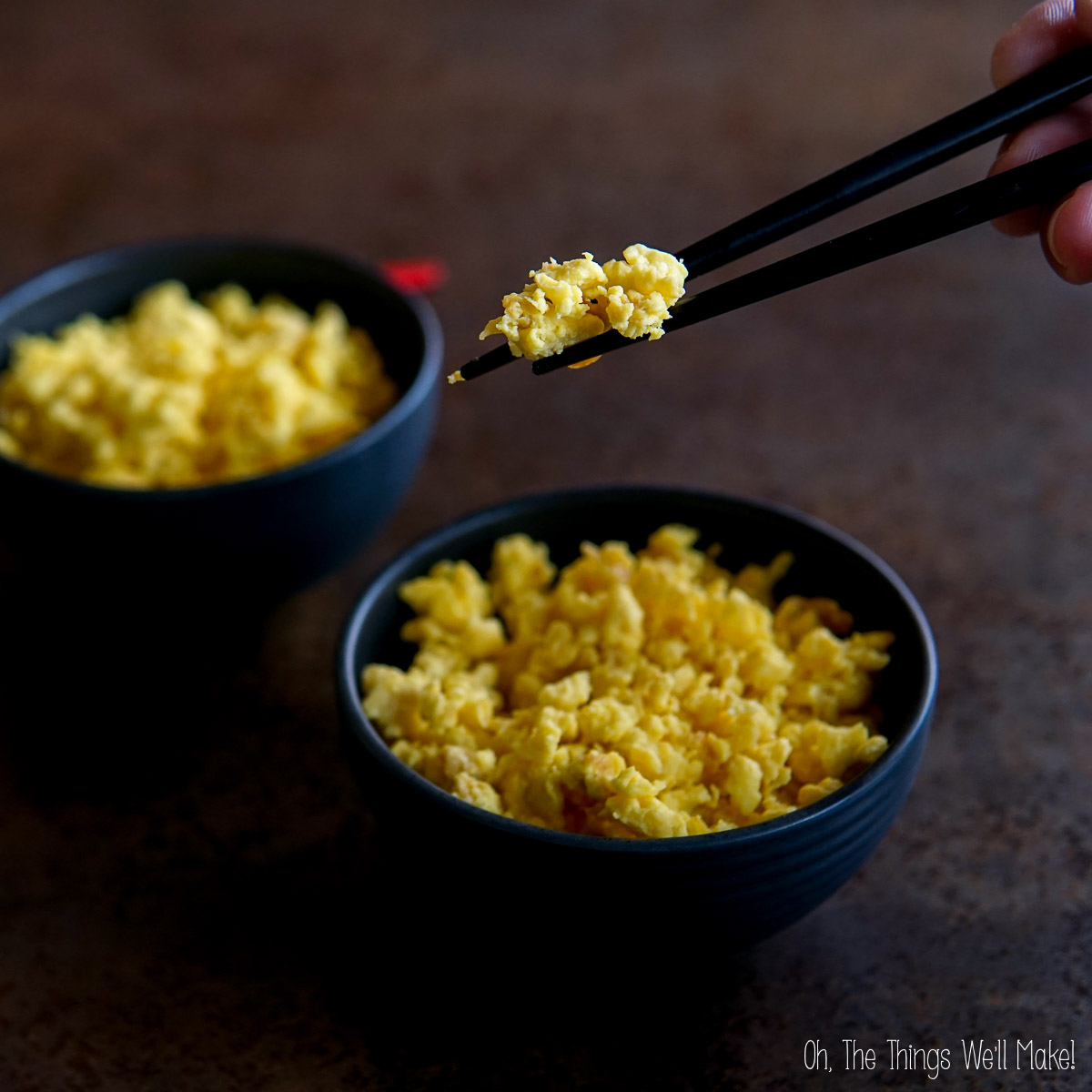 Two black bowls filled with carnivore rice, with a hand using chopsticks to pick up some from one bowl.