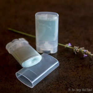 Two homemade zinc oxide sticks in clear plastic containers, one standing upright and one lying down with its lid off, with a sprig of lavender in the background.