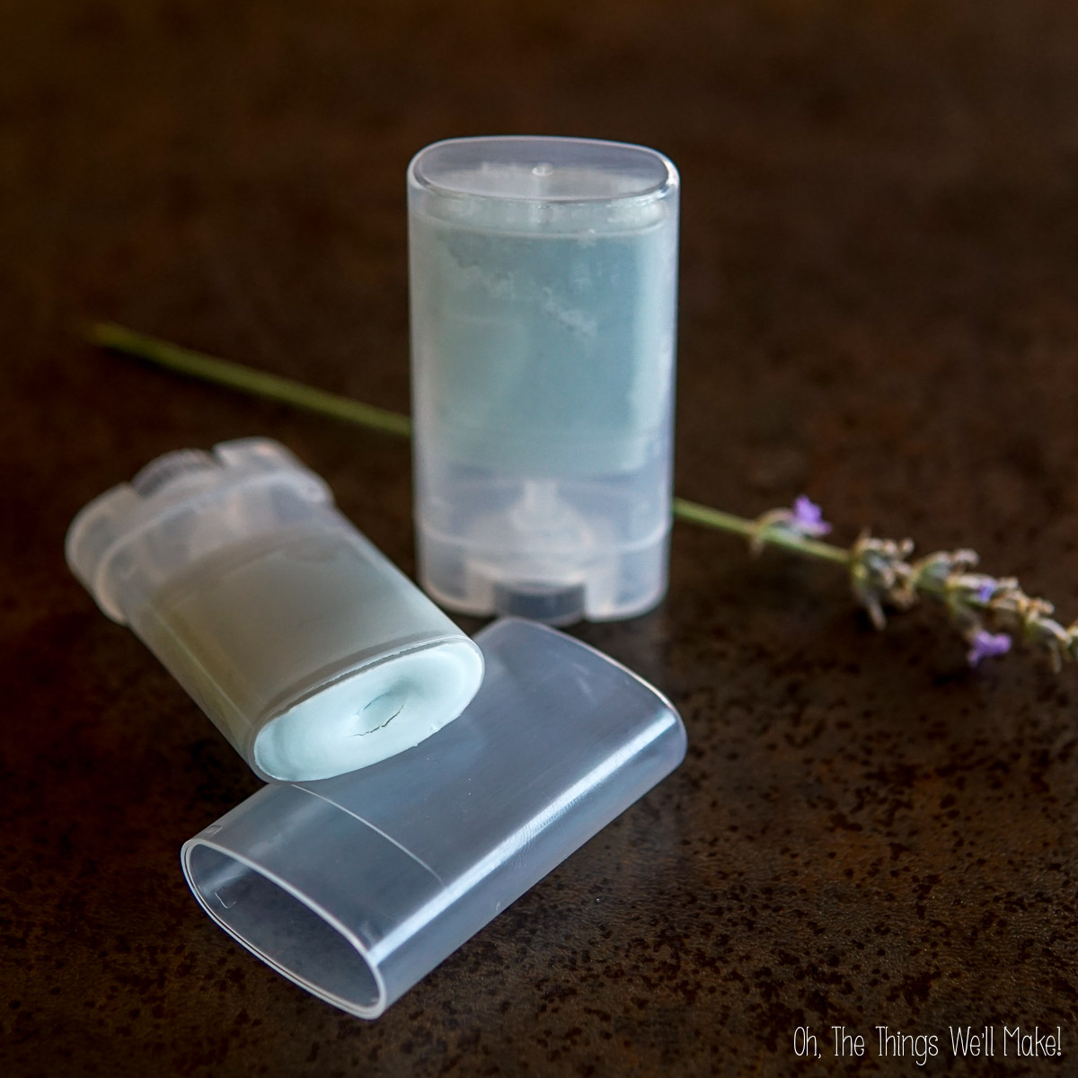 Two homemade zinc oxide sticks in clear plastic containers, one standing upright and one lying down with its lid off, with a sprig of lavender in the background.