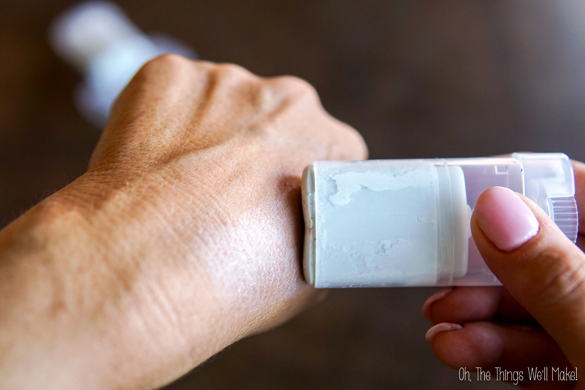 A hand holds a white solid stick applicator and applies it to the back of another hand.
