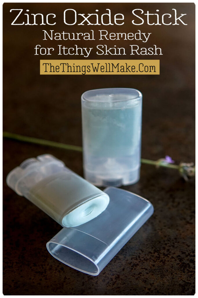 Two tubes of zinc oxide stick are displayed on a dark surface with a small flower and a label reading "Zinc Oxide Stick, Natural Remedy for Itchy Skin Rash" and "TheThingsWellMake.Com.