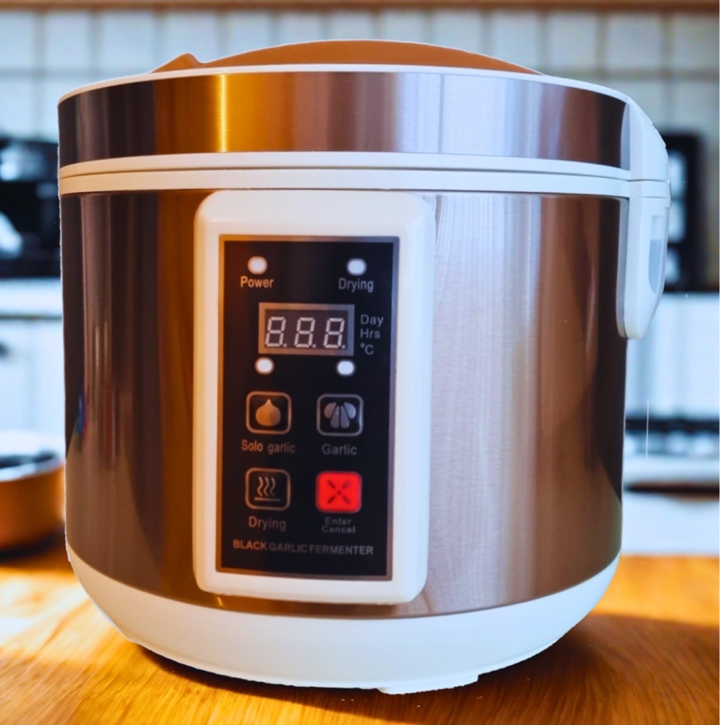 A black garlic fermenter sits on a wooden countertop.