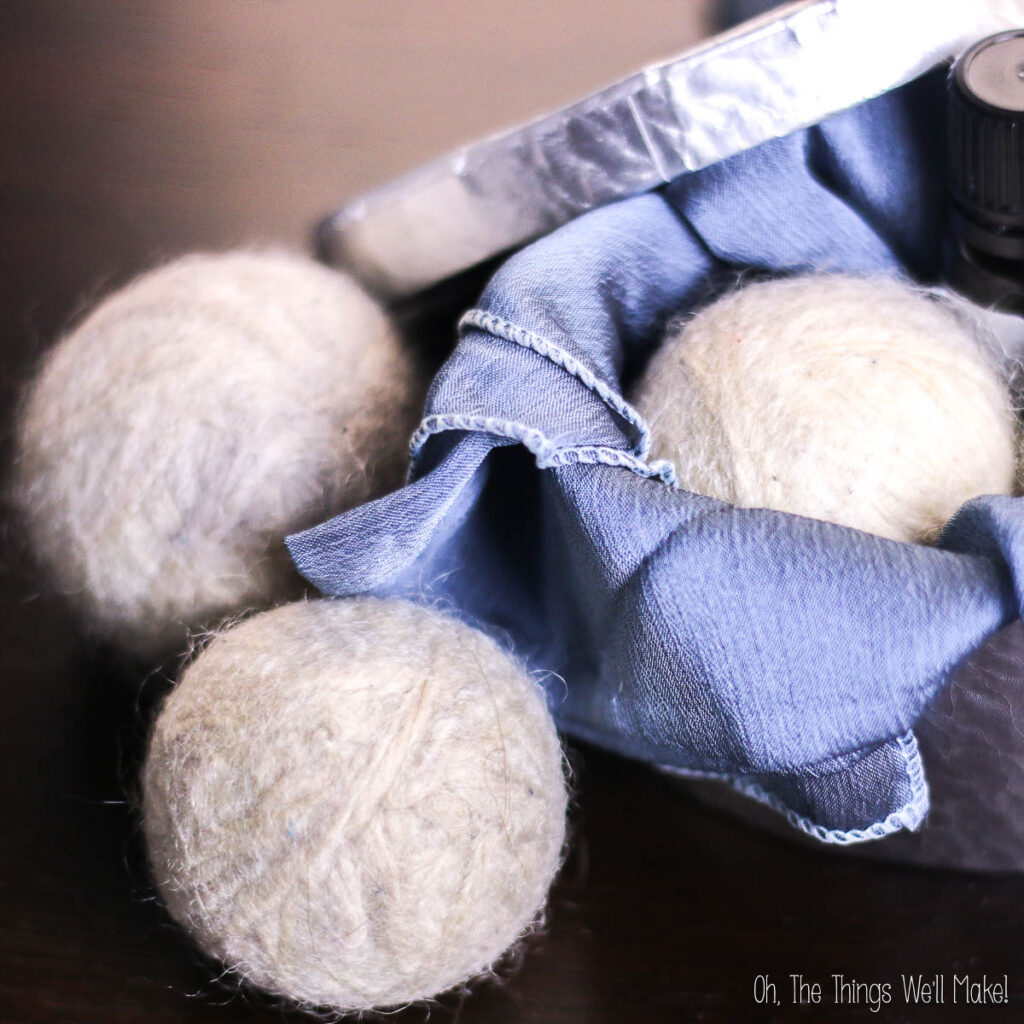 Three diy wool dryer balls sit on a table, partially wrapped in a blue cloth, with a metal container.