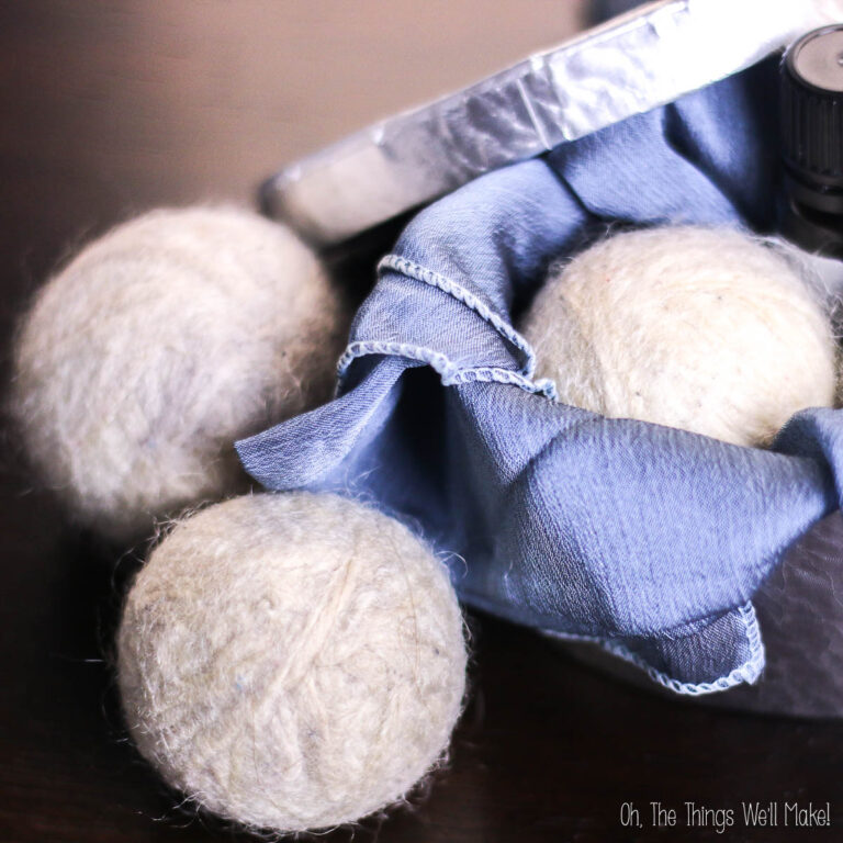 Three diy wool dryer balls sit on a table, partially wrapped in a blue cloth, with a metal container and a small bottle nearby.
