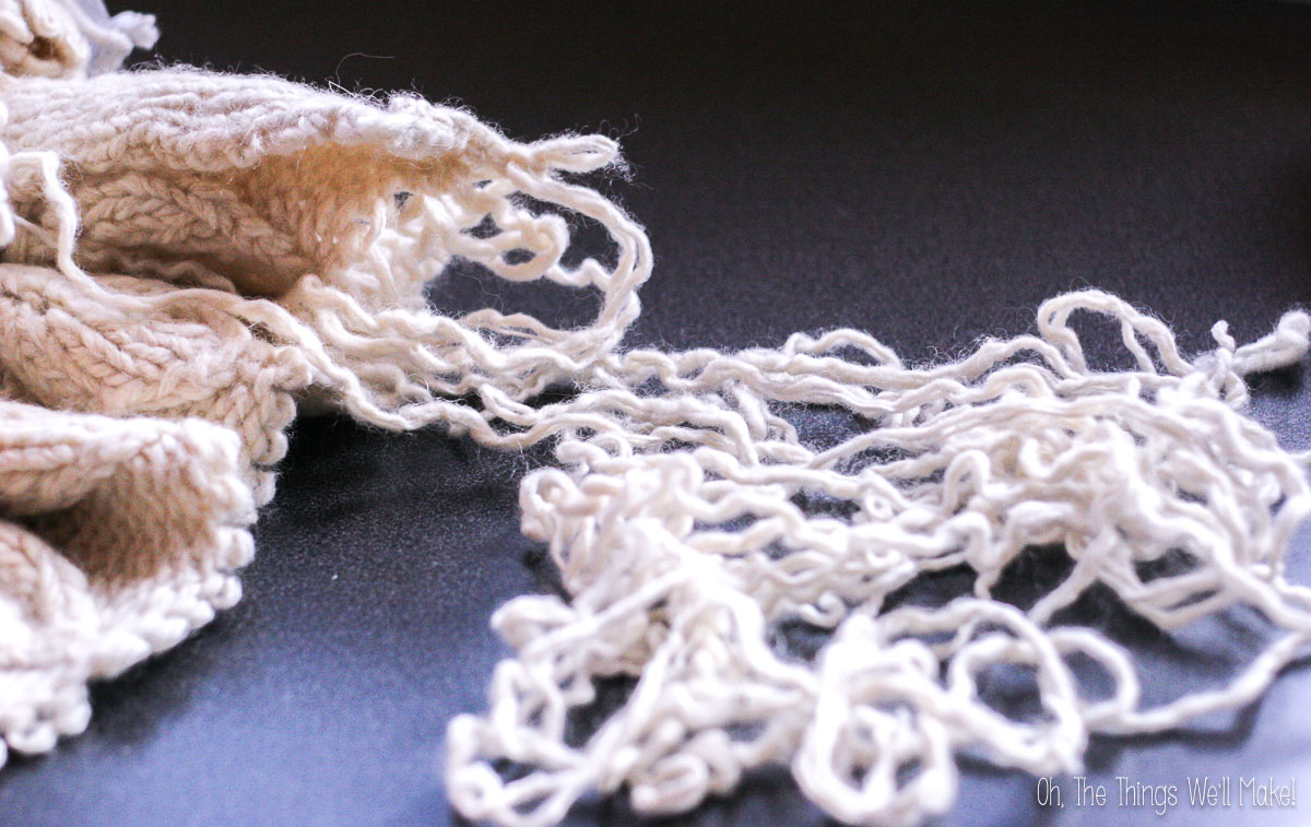 A partially unraveled wool sweater and a pile of loose, wavy yarn strands on a dark surface